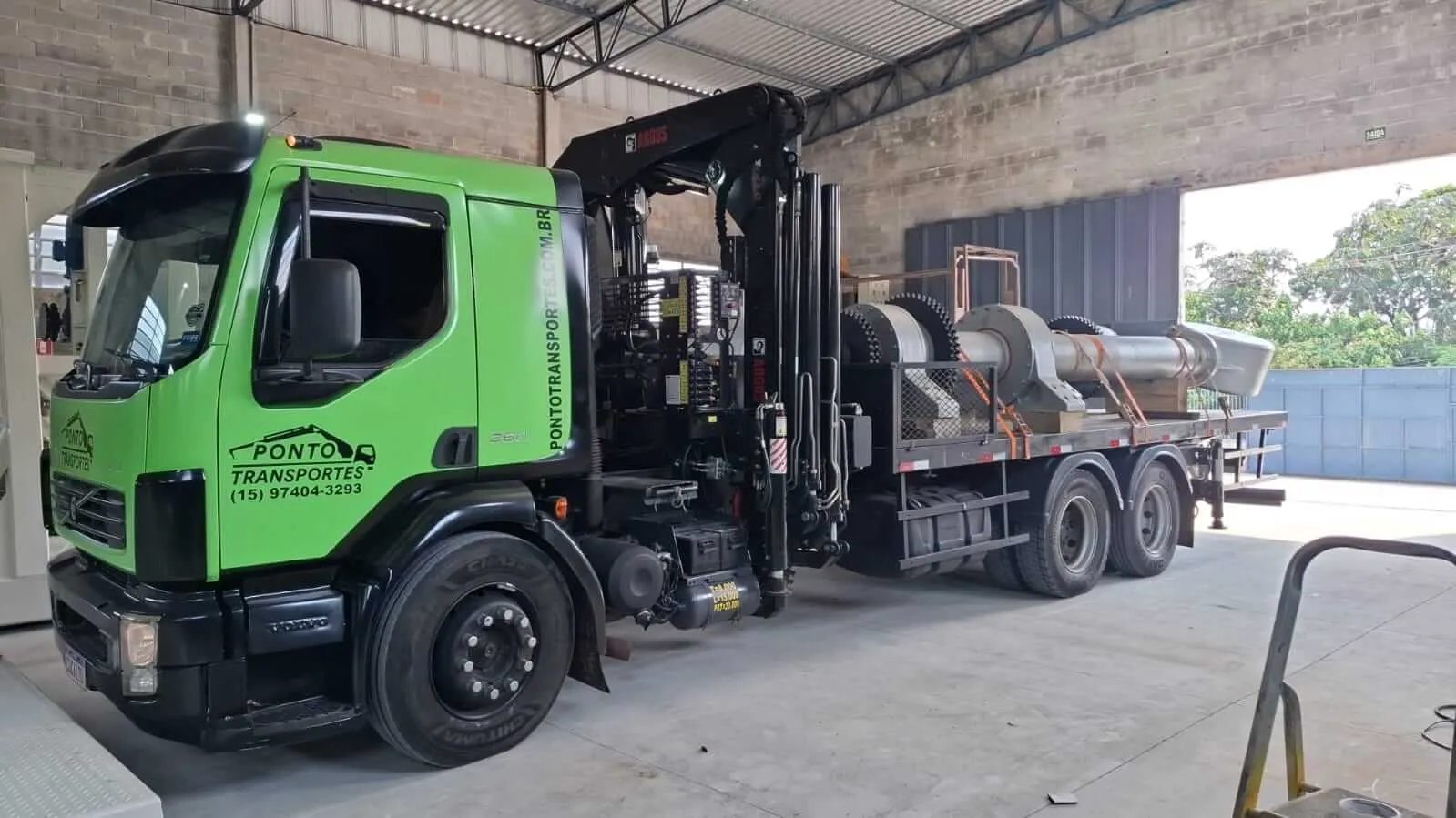 Caminhão munck transportando máquina industrial em galpão